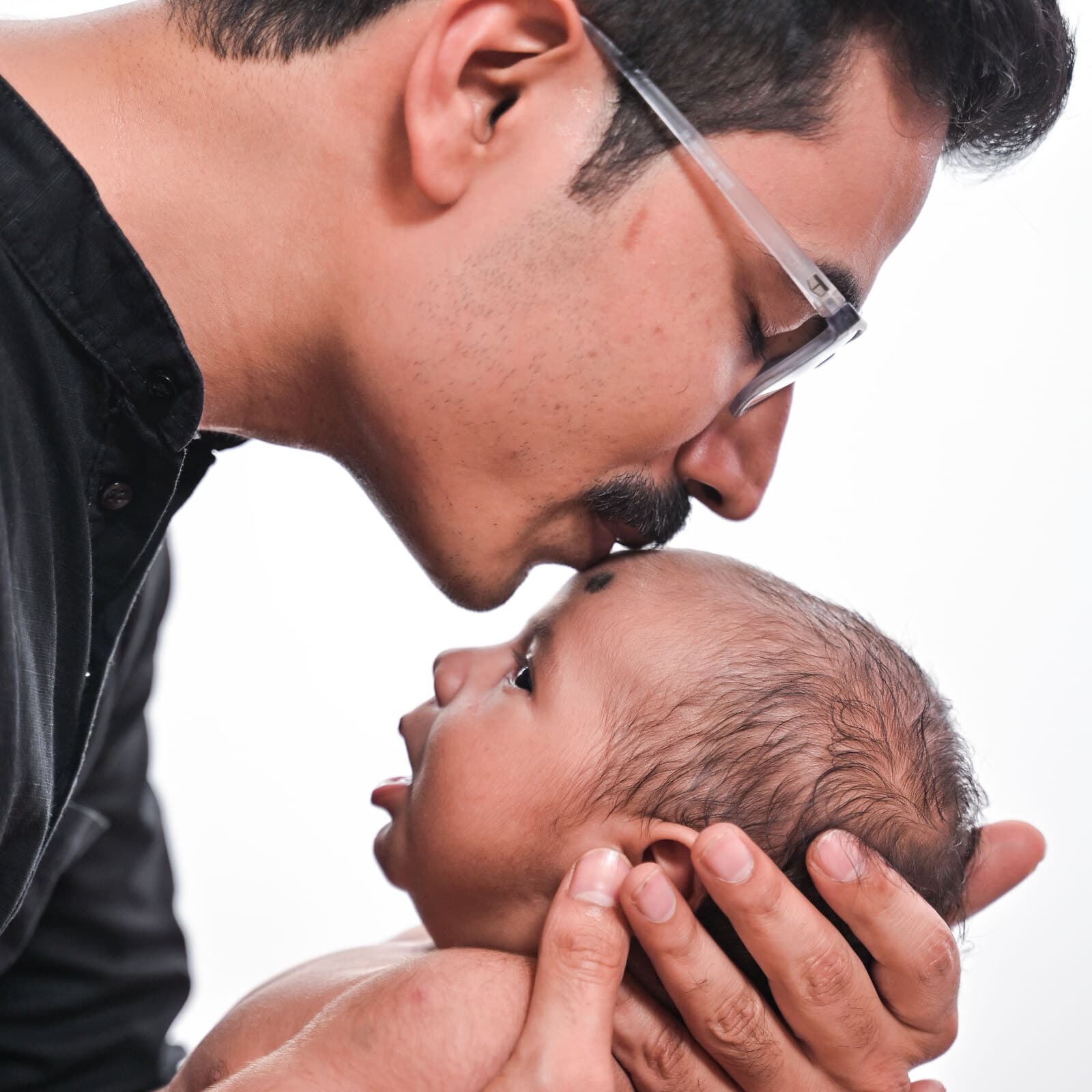 A father kissing his newborn's forehead, cradled in both hands